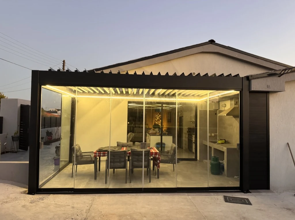 Dark aluminium bioclimatic pergola with glass enclosure and integrated lighting by Protent Cyprus